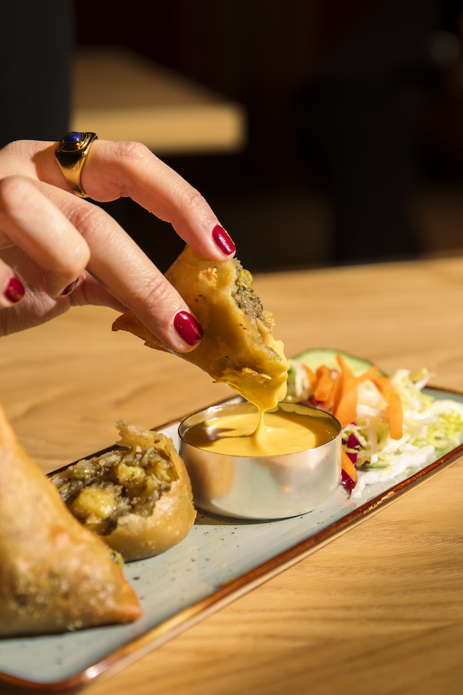 hand dipping samosa in mango sauce