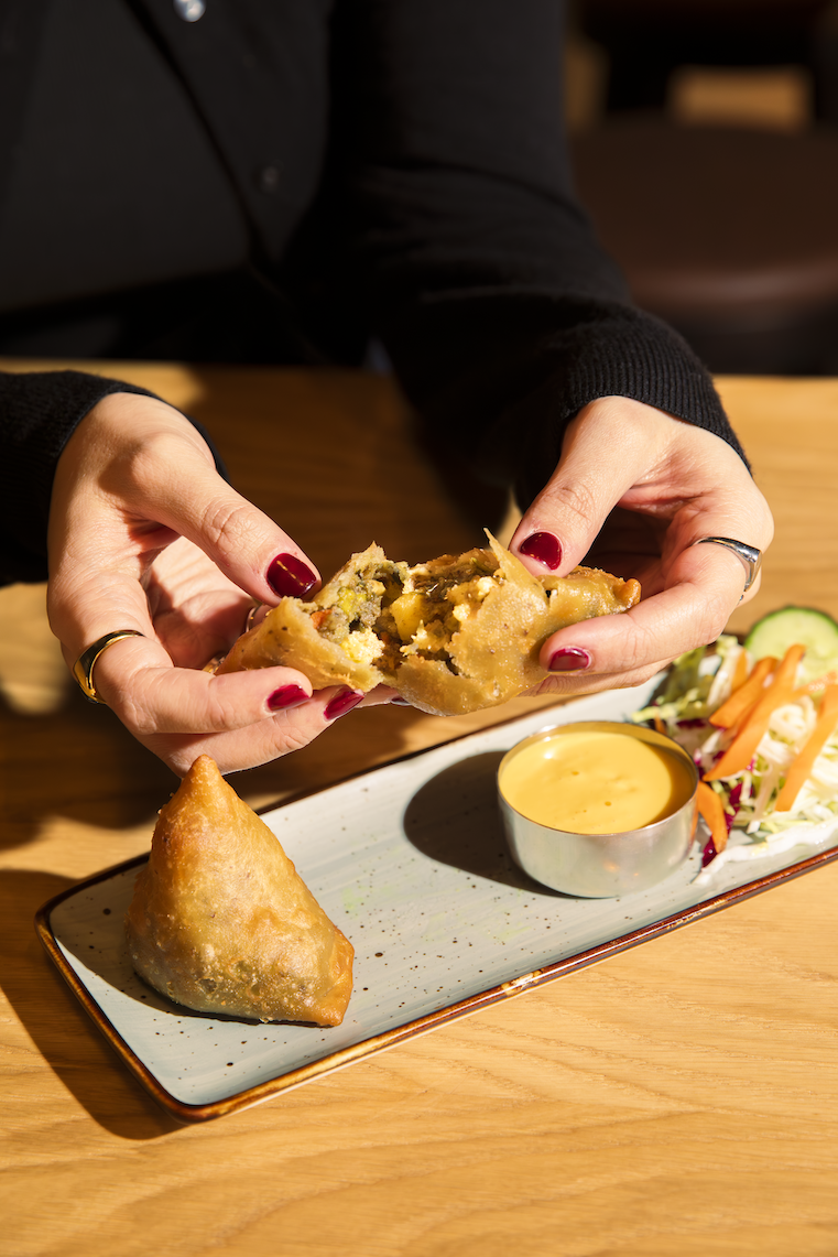 Hands splitting samosa showing filling